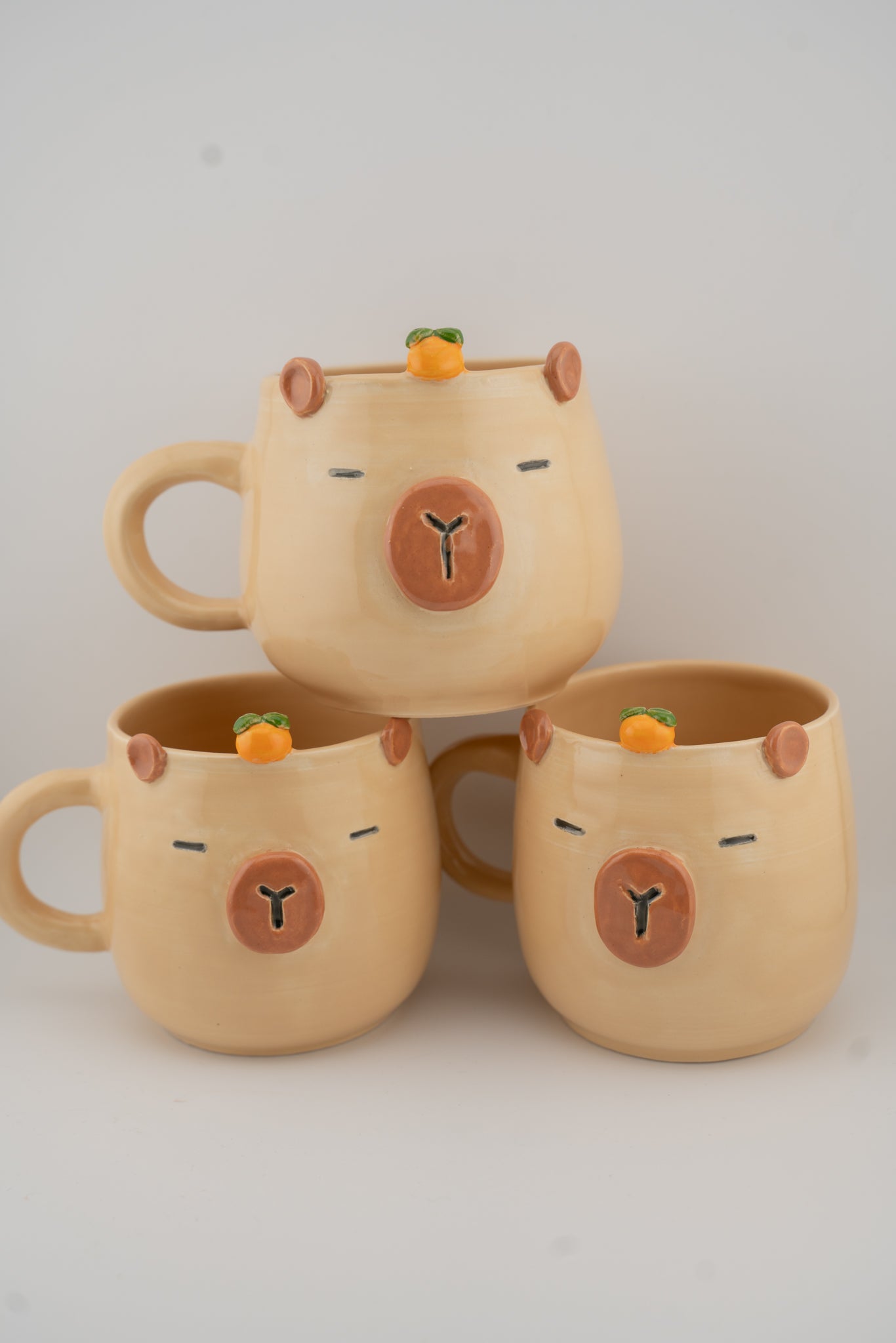 Three beige ceramic mugs with bear faces on a light gray background